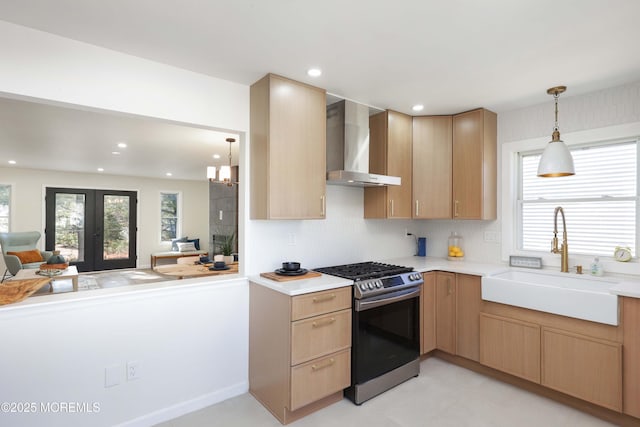 kitchen with a healthy amount of sunlight, a sink, stainless steel gas range oven, wall chimney range hood, and open floor plan