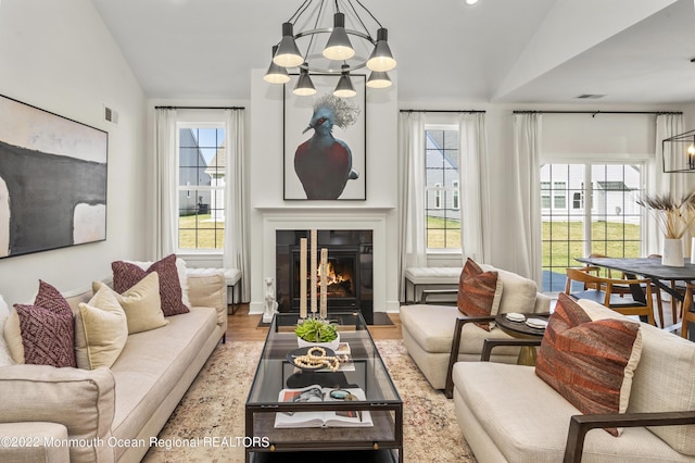 living area featuring a wealth of natural light, a fireplace with flush hearth, a notable chandelier, and vaulted ceiling