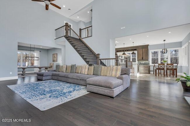 living area featuring stairs, ceiling fan with notable chandelier, wood finished floors, and baseboards