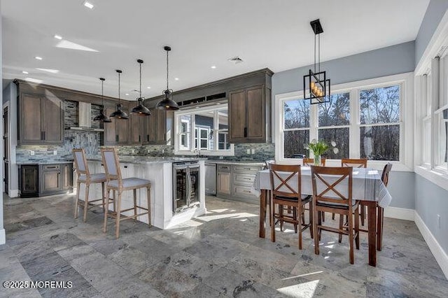 kitchen with backsplash, a center island, wine cooler, dark brown cabinetry, and wall chimney exhaust hood