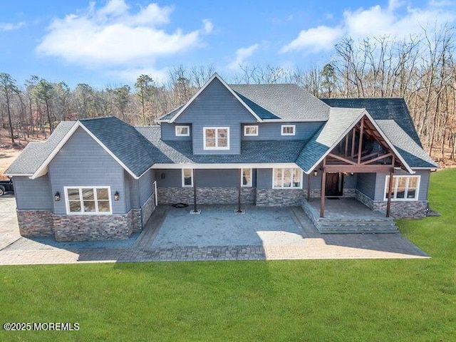 back of property with a yard, stone siding, and a shingled roof