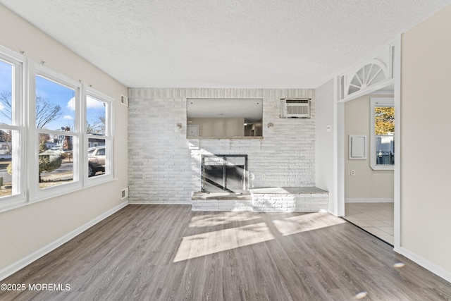 unfurnished living room featuring baseboards, a fireplace, wood finished floors, a textured ceiling, and a wall mounted AC