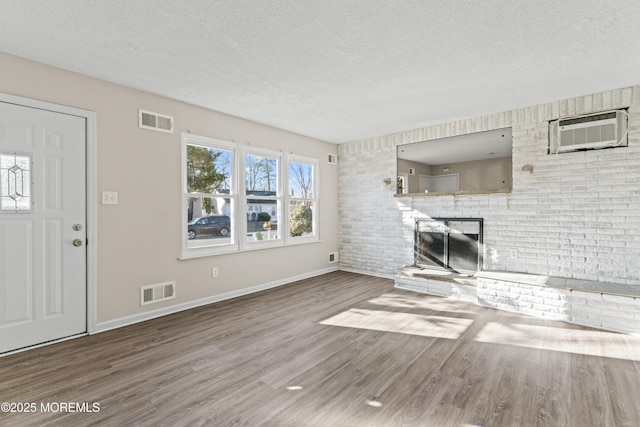 unfurnished living room with visible vents, a textured ceiling, an AC wall unit, and a fireplace