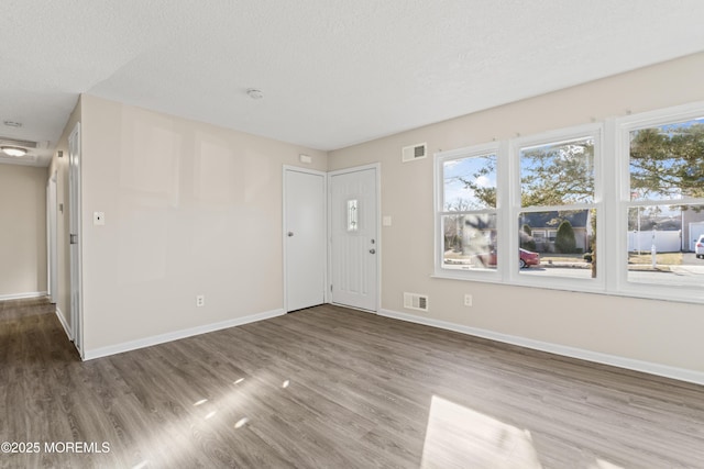 interior space with visible vents, a textured ceiling, baseboards, and wood finished floors