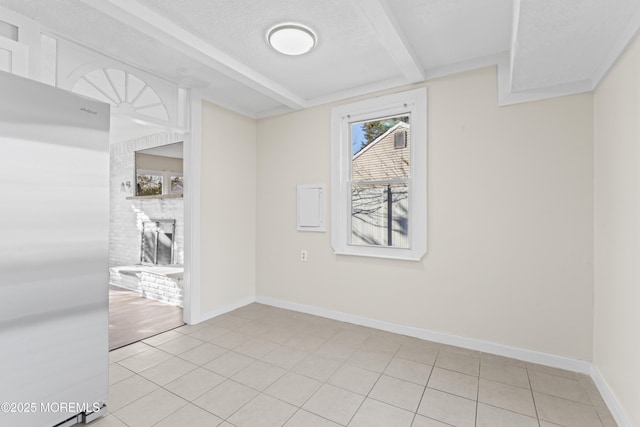 spare room with light tile patterned floors, beamed ceiling, baseboards, a textured ceiling, and a brick fireplace