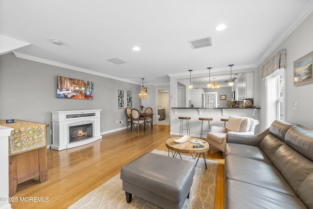 living area with baseboards, visible vents, a fireplace, crown molding, and light wood-type flooring