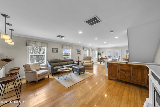 living area with ornamental molding, visible vents, and light wood-type flooring