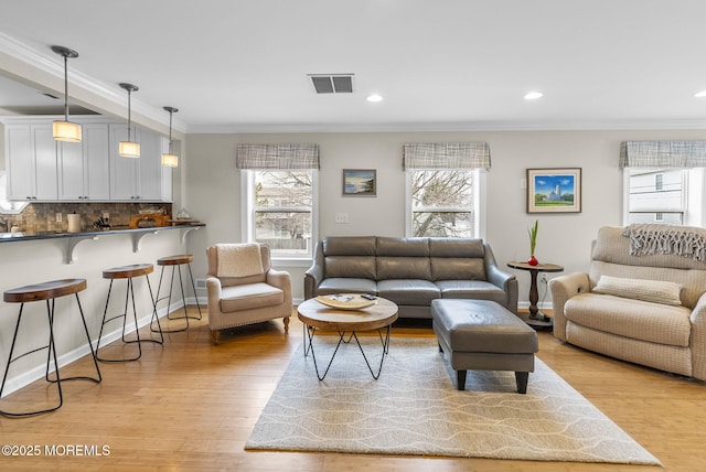 living room with visible vents, a healthy amount of sunlight, ornamental molding, and light wood finished floors