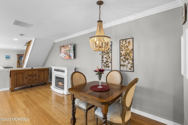 dining space featuring a glass covered fireplace, baseboards, visible vents, and light wood-type flooring