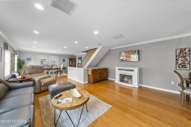 living room featuring stairs, light wood finished floors, visible vents, and a high end fireplace