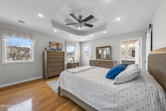 bedroom with visible vents, recessed lighting, a barn door, light wood finished floors, and a raised ceiling