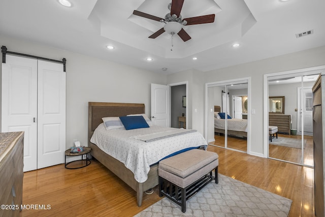 bedroom with visible vents, multiple closets, a tray ceiling, a barn door, and light wood-style floors