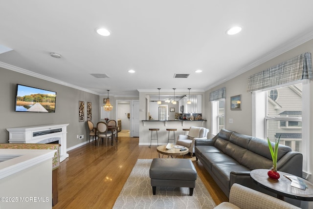 living room featuring wood finished floors, crown molding, a fireplace, and visible vents