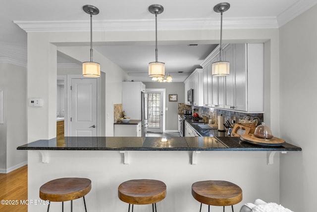 kitchen with light wood-type flooring, appliances with stainless steel finishes, a peninsula, crown molding, and decorative backsplash