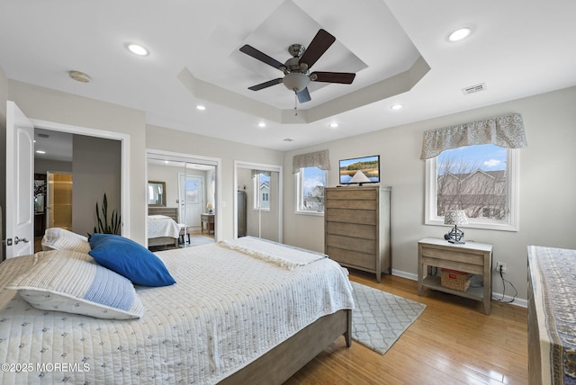 bedroom with visible vents, light wood finished floors, baseboards, a tray ceiling, and recessed lighting