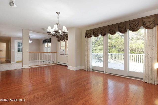 spare room with a baseboard heating unit, wood finished floors, baseboards, and a chandelier