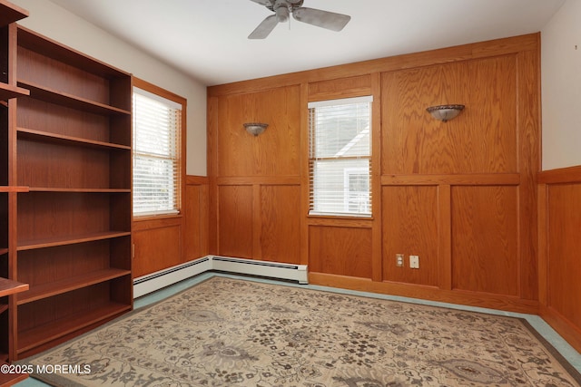 empty room featuring a baseboard heating unit, a wainscoted wall, wood walls, and ceiling fan