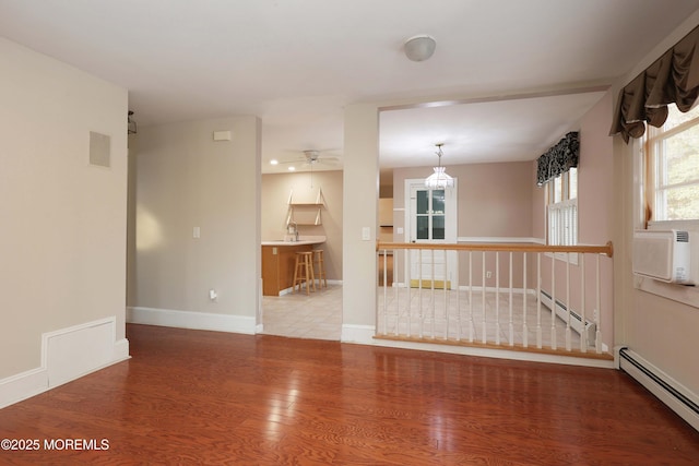 unfurnished room featuring a baseboard radiator, baseboards, wood finished floors, and ceiling fan with notable chandelier