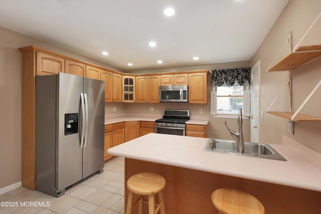 kitchen with a peninsula, a sink, stainless steel appliances, glass insert cabinets, and a kitchen bar