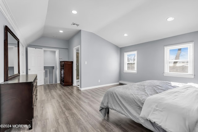 bedroom with baseboards, visible vents, light wood finished floors, lofted ceiling, and a baseboard heating unit