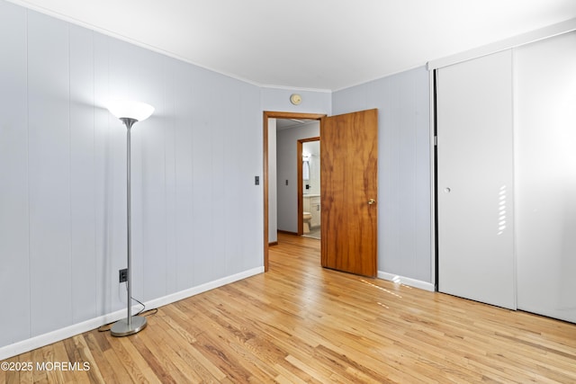 unfurnished bedroom with a closet, baseboards, light wood-style floors, and ornamental molding