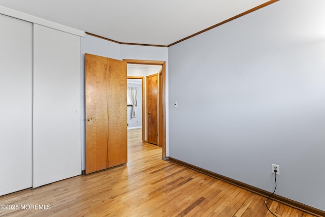 unfurnished bedroom featuring a closet, light wood-type flooring, baseboards, and ornamental molding