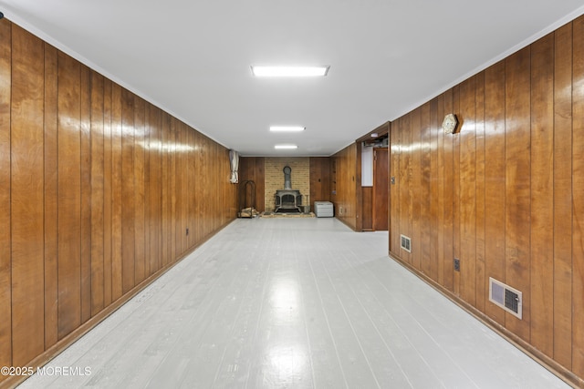 finished basement featuring visible vents, wood walls, a wood stove, and light wood-style floors