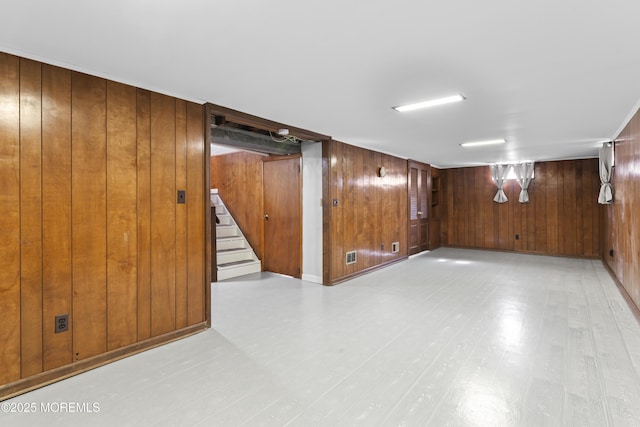 finished basement featuring wooden walls, visible vents, stairs, and light wood-style floors