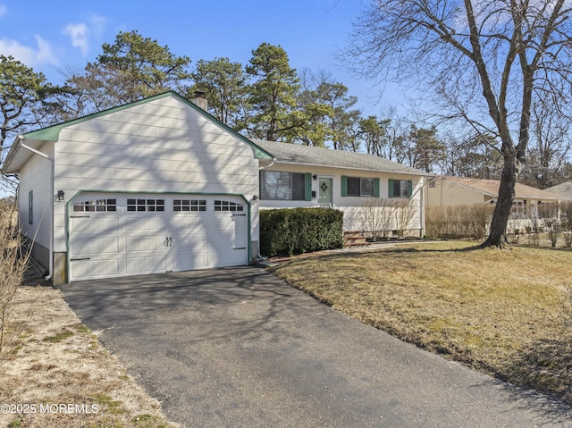 view of front facade with aphalt driveway, an attached garage, a front lawn, and a chimney