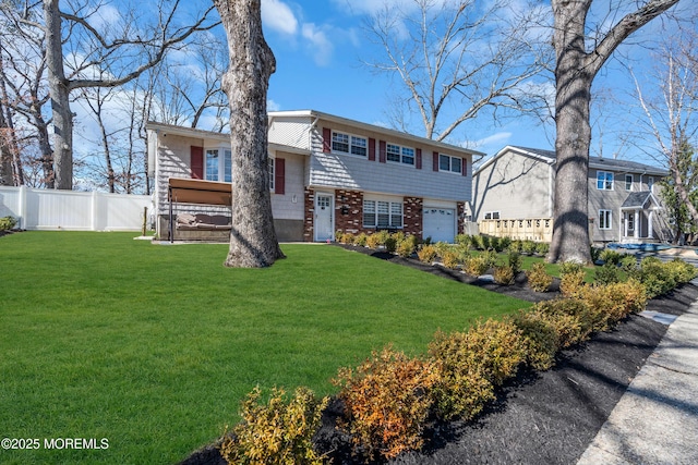 split level home with a front yard, an attached garage, fence, and brick siding