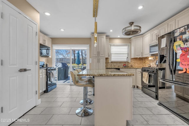 kitchen with light stone countertops, a kitchen island, a sink, black appliances, and backsplash