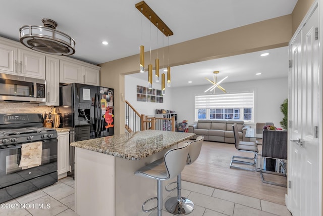 kitchen featuring tasteful backsplash, a kitchen island, light stone counters, a kitchen breakfast bar, and black appliances