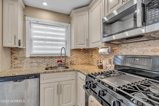 kitchen featuring a sink, light stone counters, backsplash, white cabinetry, and appliances with stainless steel finishes