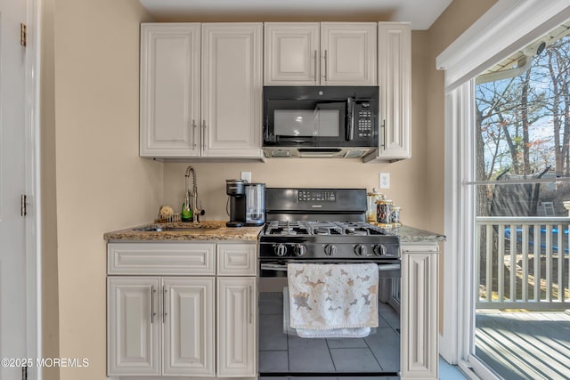 kitchen with white cabinetry, black appliances, light stone counters, and a sink