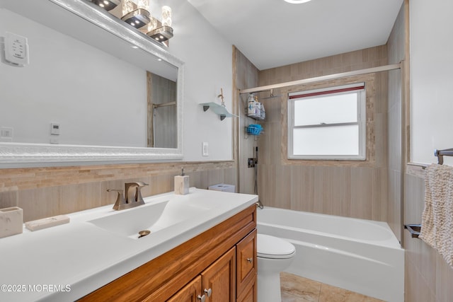 full bathroom featuring tub / shower combination, toilet, vanity, wainscoting, and tile walls