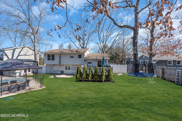 back of house featuring a fenced in pool, a fenced backyard, a deck, a trampoline, and a lawn