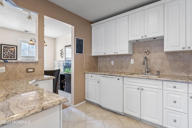 kitchen with visible vents, a sink, light stone counters, white dishwasher, and light tile patterned floors