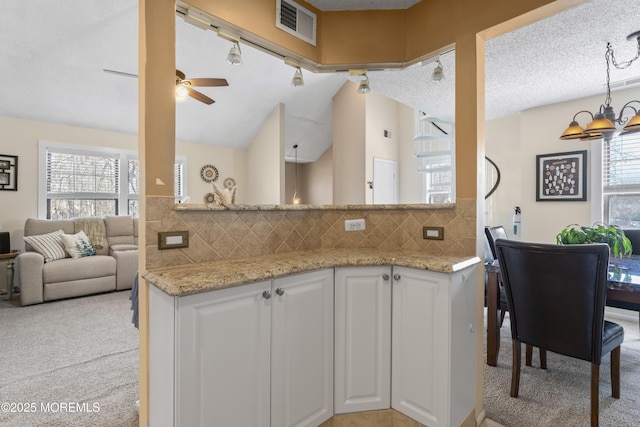 kitchen with visible vents, light colored carpet, vaulted ceiling, light stone counters, and white cabinets