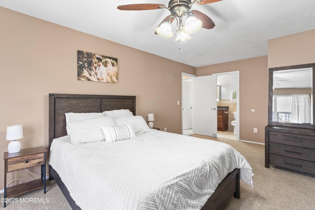 bedroom featuring baseboards, light colored carpet, a textured ceiling, ensuite bath, and a ceiling fan