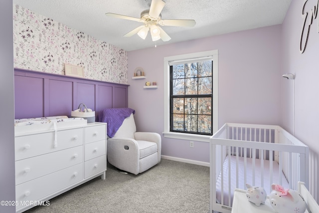 bedroom featuring a wainscoted wall, carpet floors, wallpapered walls, a crib, and a textured ceiling