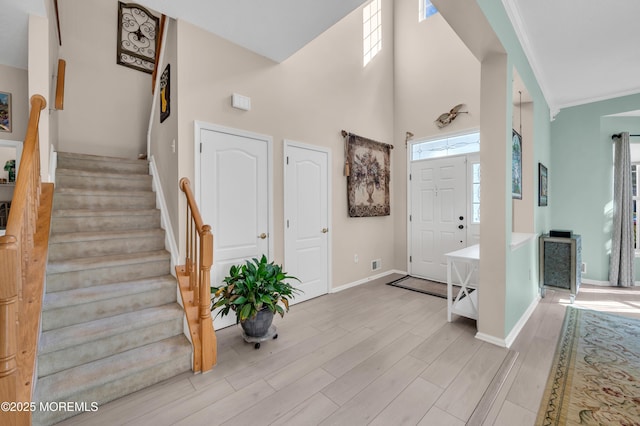 foyer entrance with baseboards, light wood-style floors, a high ceiling, and stairs