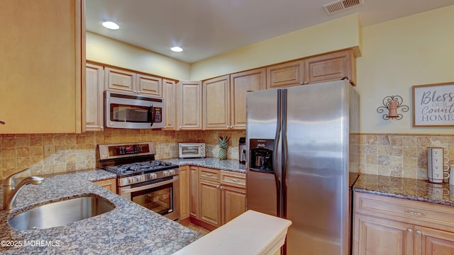 kitchen featuring visible vents, a sink, tasteful backsplash, stainless steel appliances, and stone counters