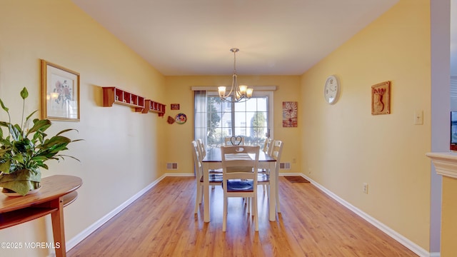 dining space featuring visible vents, light wood-style flooring, baseboards, and an inviting chandelier