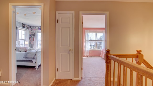 corridor with an upstairs landing, light colored carpet, baseboards, and a healthy amount of sunlight