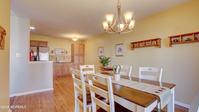 dining room with light wood-type flooring, baseboards, and an inviting chandelier