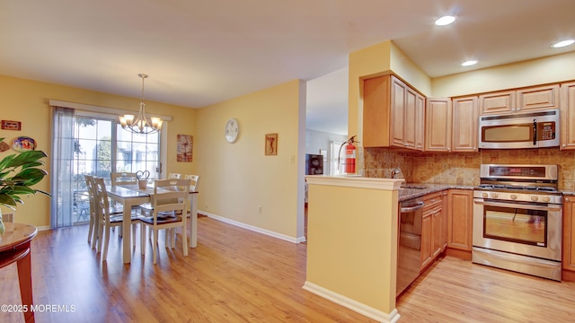 kitchen featuring tasteful backsplash, appliances with stainless steel finishes, light wood finished floors, light stone countertops, and a chandelier