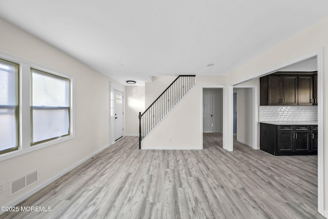 unfurnished living room with light wood-type flooring, visible vents, baseboards, and stairs