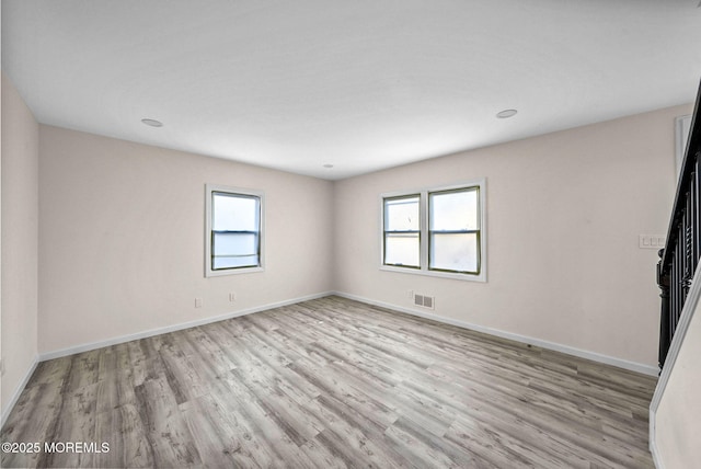 empty room with plenty of natural light, baseboards, visible vents, and wood finished floors