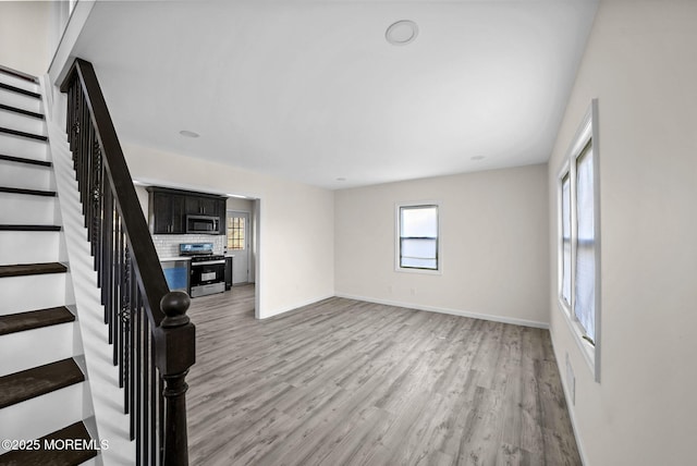 unfurnished living room with stairway, light wood-type flooring, and baseboards