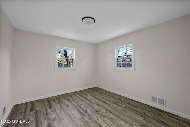 spare room with wood finished floors, a healthy amount of sunlight, visible vents, and baseboards